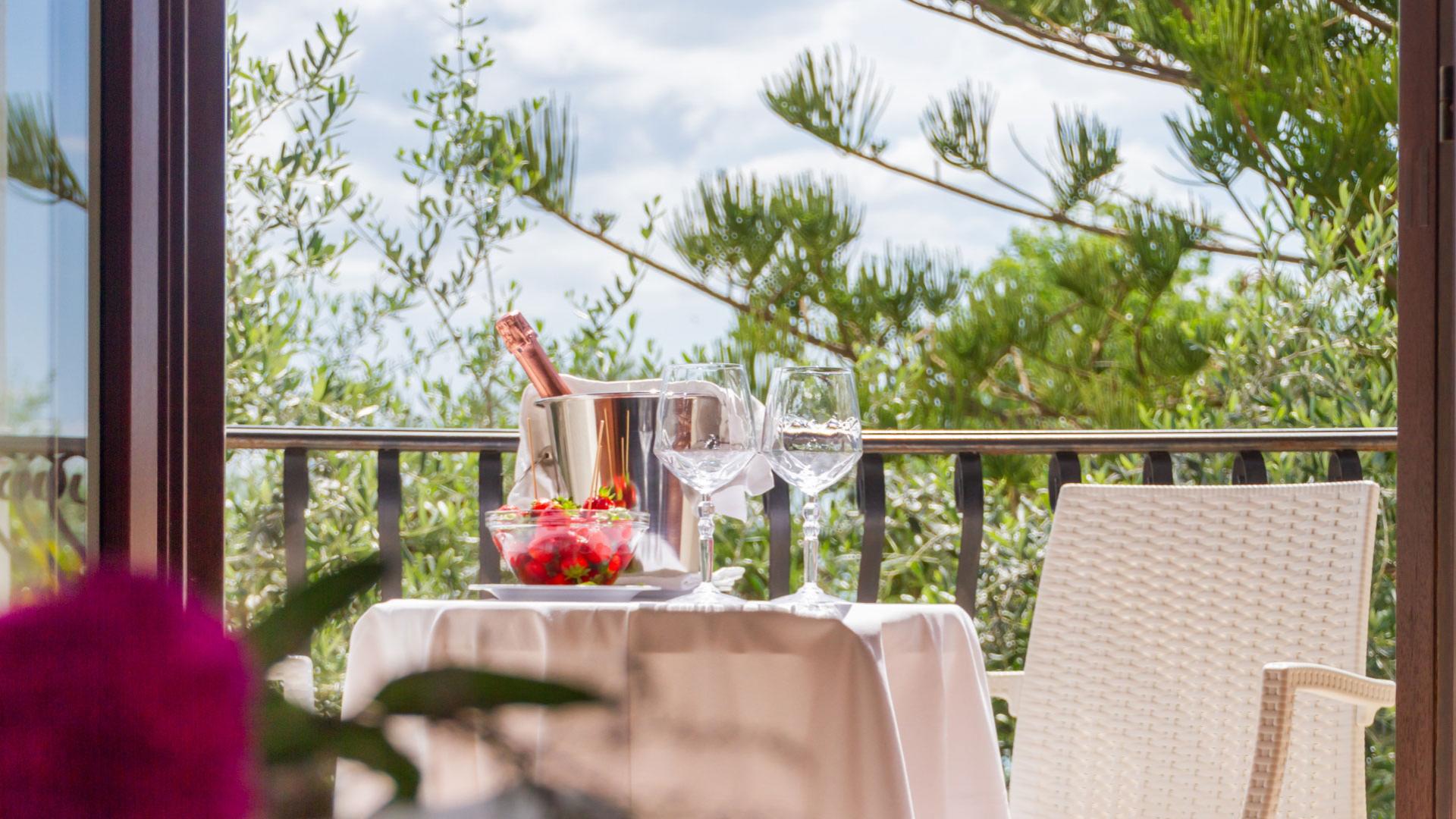 Tavolo all'aperto con champagne, fragole e bicchieri, vista su alberi verdi.