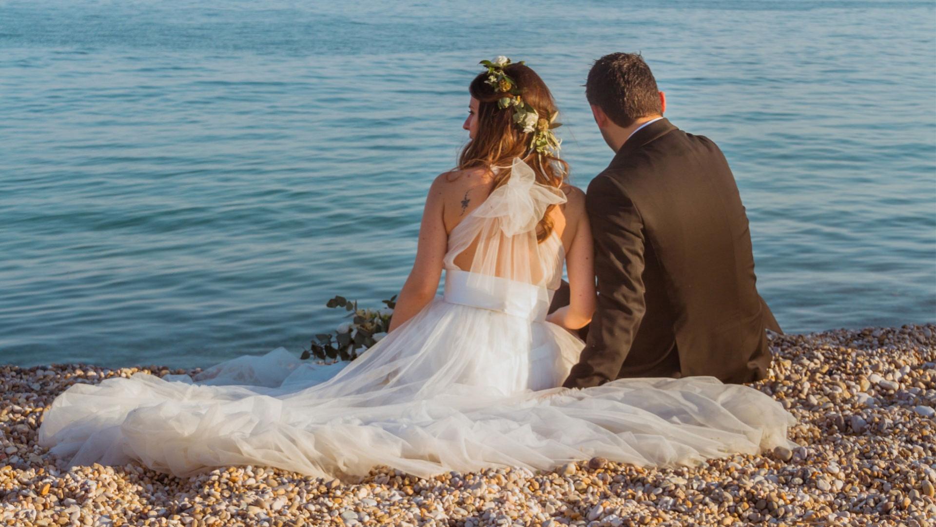 Una coppia di sposi seduta sulla spiaggia, guardando il mare.