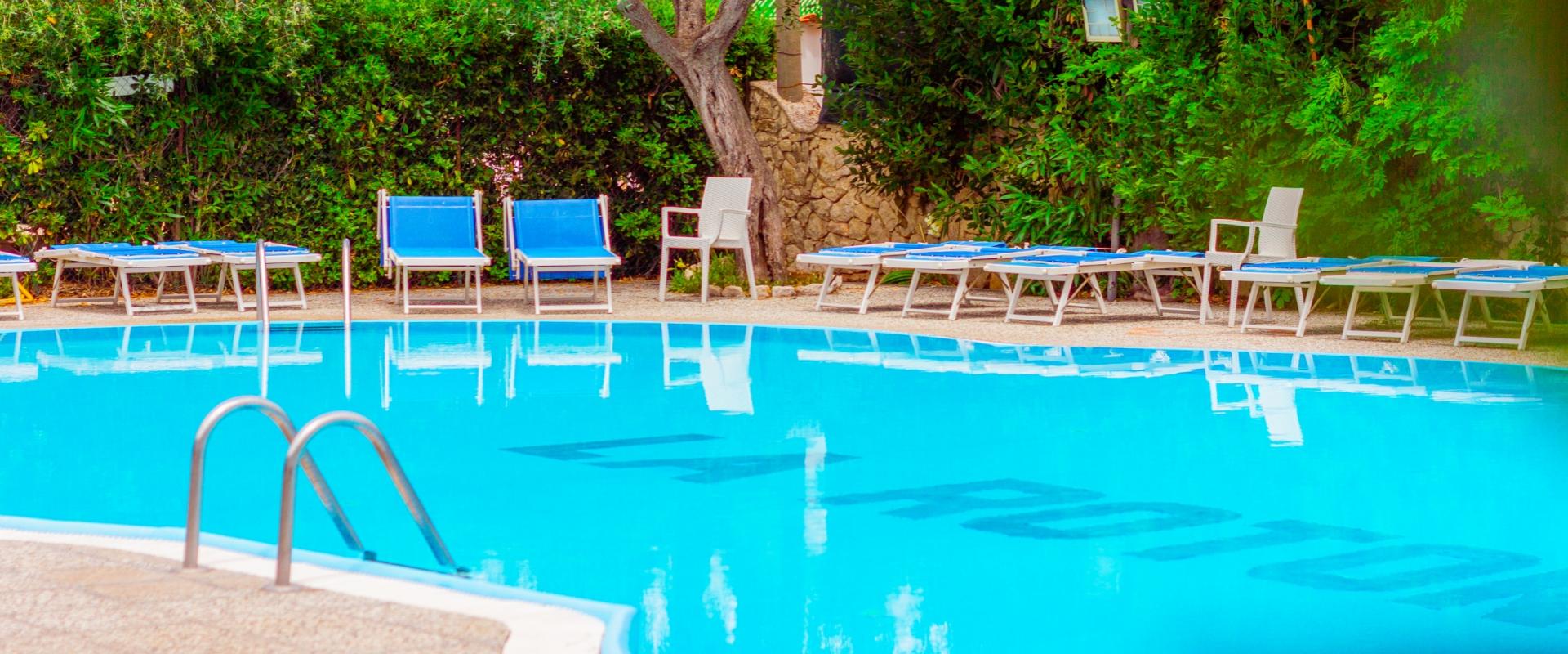 Piscina all'aperto con lettini blu e verde vegetazione circostante.