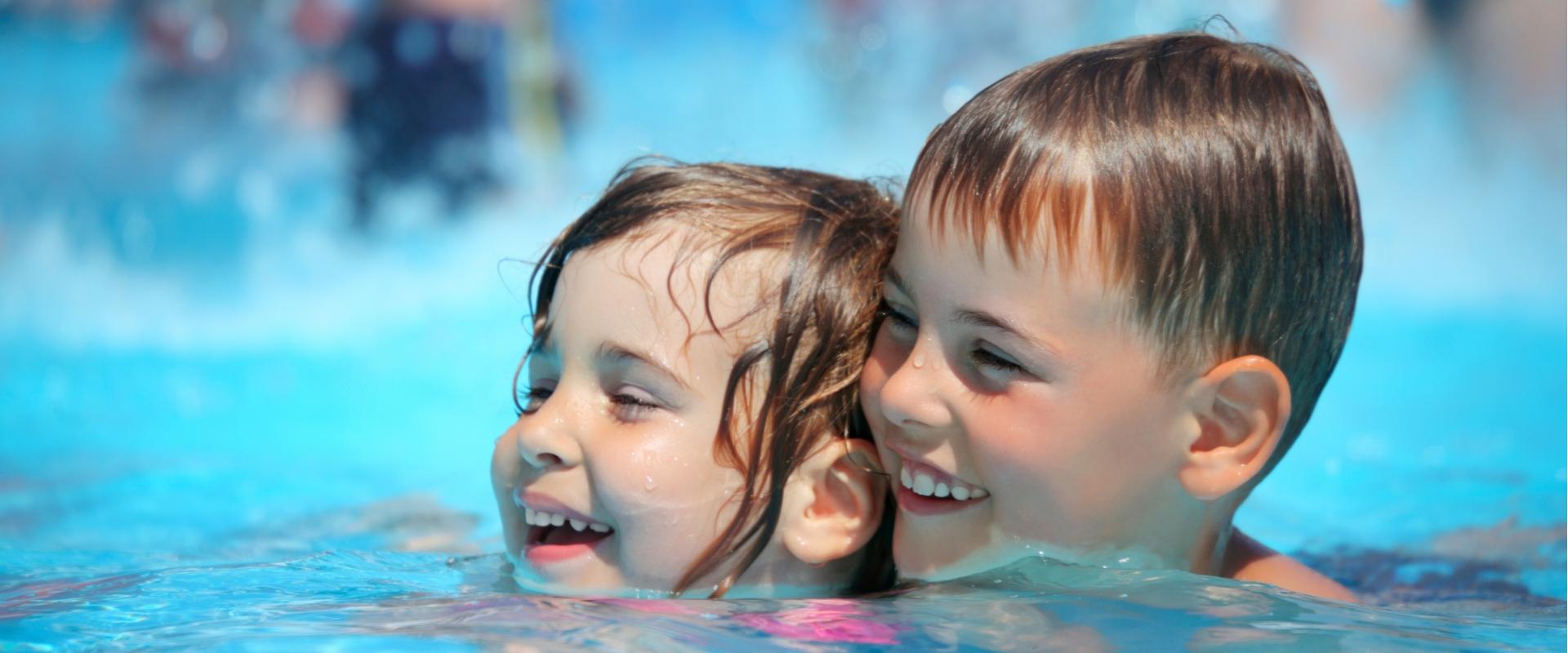 Due bambini sorridenti che nuotano e giocano insieme in piscina.