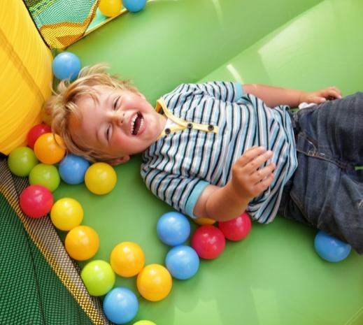 Bambino sorridente gioca in una piscina di palline colorate, divertendosi moltissimo.