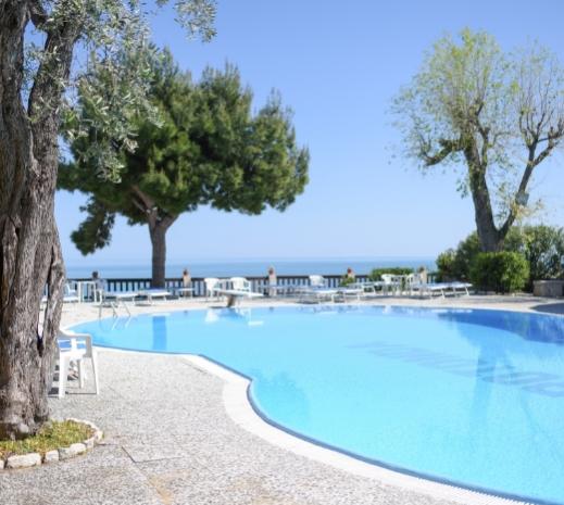 Piscina all'aperto con vista mare, circondata da alberi e sedie a sdraio.