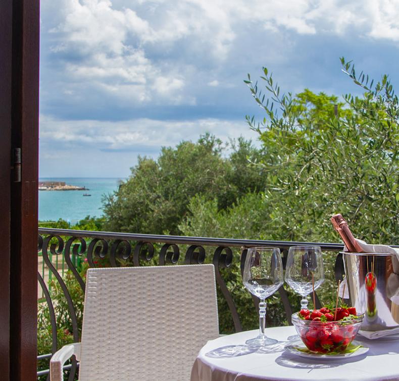 Vista mare con tavolo apparecchiato, champagne e fragole su un balcone.