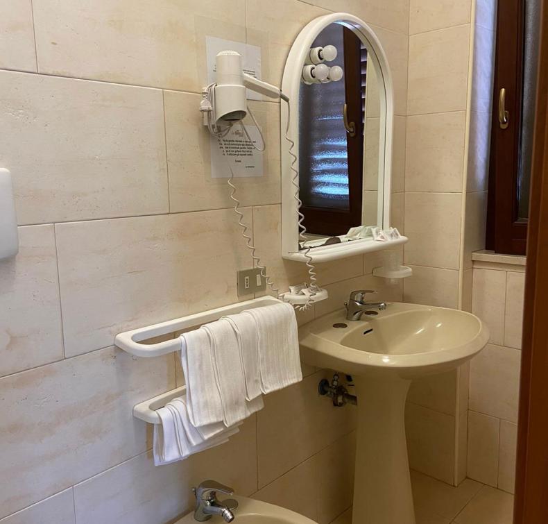 Bagno con lavabo, bidet, specchio, asciugacapelli e asciugamani bianchi su portasciugamani.