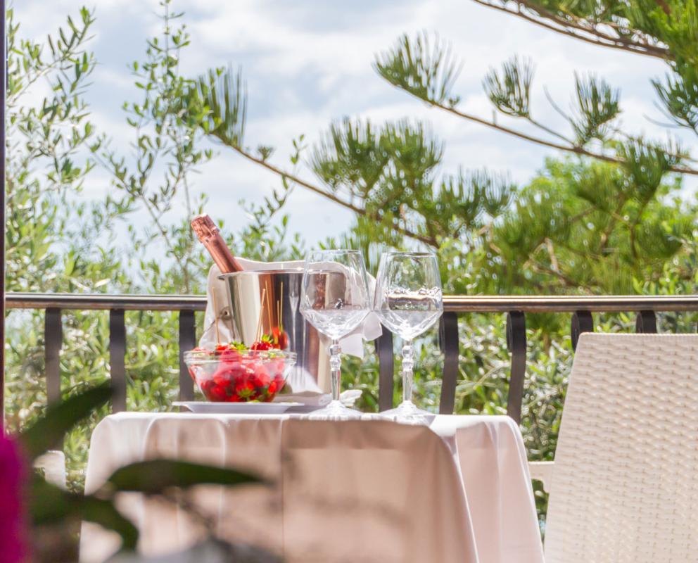 Tavolo all'aperto con champagne, fragole e bicchieri, vista su alberi verdi.